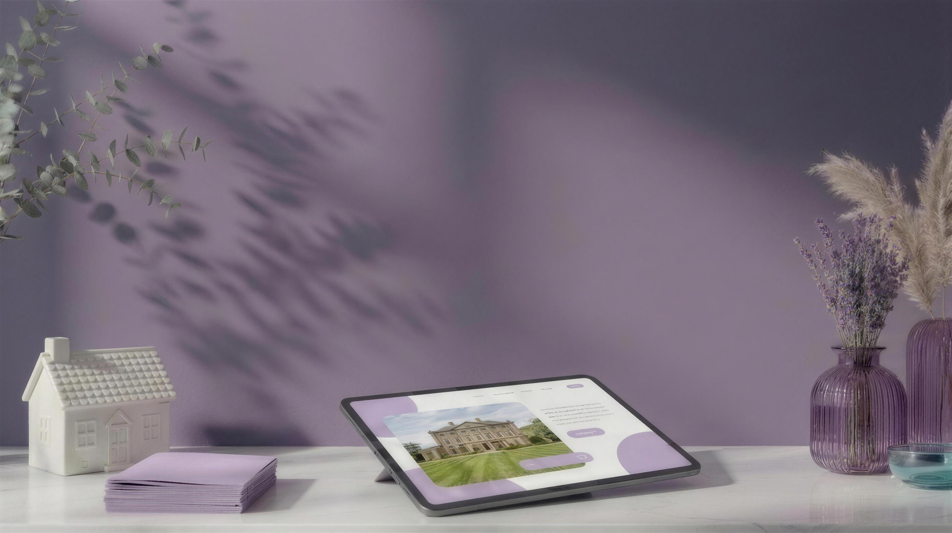 Estate agent website design scene: ceramic cottage, brochures and a tablet showing a property website against a grey wall